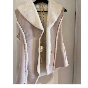 Beige pälsväst med vit fuskpäls - Snygg beige väst med vit fuskpäls längs krage och kanter. Västen har en öppen design och markerade sömmar som ger en cool look. Perfekt för lager-på-lager och att lyfta vilken outfit som helst.