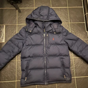 Mörkblå dunjacka från Polo Ralph Lauren - Snygg mörkblå dunjacka från Polo Ralph Lauren. Säljer den då jag växt ur den, haft den i cirka 1 år och köpte den från Ralph Laurens hemsida för cirka 2400kr.