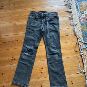Svarta jeans från Nudie Jeans, W34 L34 - Snygga svarta jeans från Nudie Jeans med klassisk femficksdesign och subtila broderade detaljer på bakfickorna. Modellen har rak passform och normal midja, tillverkade i slitstarkt bomullsmaterial. Perfekt för dig som gillar stilrena och tidlösa jeans.