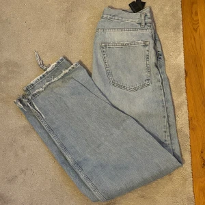 Ljusa raka jeans från Zara - Säljer ett par ljusblå jeans från Zara med rak passform och hög midja. Jeansen har klassiska fem fickor och rå, fransig kant nedtill för en cool och avslappnad vibe. Perfekta för dig som gillar en loose och trendig stil.