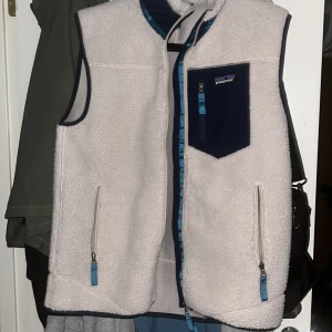  Patagonia väst - Säljer en vit fleeceväst från Patagonia i storlek M. Västen har marinblå detaljer, dragkedja framtill och tre fickor med blå zip-pullers. Mjuk och skön med kontrastfärgad bröstficka och kantband. Perfekt för lager-på-lager under kyliga dagar. Nytt sick har knappt använt det!