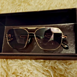 Pilotbågar med svart ram tonade glas  - Helt nya solglasögon i box med guldiga pilotbågar och svarta skalmar. Glasen är lätt tonade i brunt och har en cool geometrisk form. Detaljer i guld på skalmarna ger en lyxig känsla. Perfekt accessoar för att lyfta din stil.