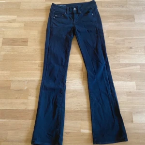 Svarta Midge Saddle bootcut jeans - Snygga svarta jeans från G-Star RAW, modellen Midge Saddle med midwaist och bootcut. Jeansen har klassiska fem fickor, dubbla knappar bak i midjan och är tillverkade i stretchig bomull för skön passform. Perfekt för dig som gillar en smal siluett med lite utsvängda ben.