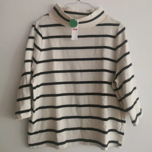 Randig halvpolotröja från Lindex XS - Snygg randig polotröja från Lindex i vitt och svart. Tröjan har en hög krage och trekvartsärm. Tillverkad i mjuk bomull som känns skön mot huden. Enkel och stilren design som funkar året runt.