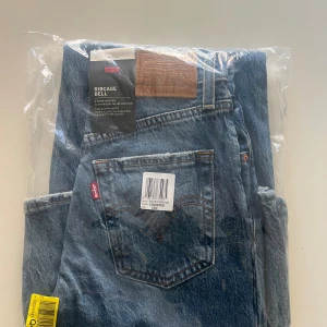 Levi's Ribcage Bell blå jeans - Snygga Levi's Ribcage Bell jeans i klassisk blå tvätt med hög midja och utsvängda ben. Jeansen har den ikoniska läderpatchen bak och röd Levi's-tag på fickan. Perfekt för dig som gillar retrovibbar och vill ha ett statement-plagg i garderoben.