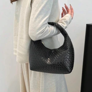 Svart axelväska i skinnimitation - Snygg svart axelväska med trendig, rundad form och präglat mönster som ger en lyxig känsla. Väskan har ett kort handtag och är tillverkad i skinnimitation med reptilstruktur. Perfekt accessoar för att lyfta din outfit. Aldrig använd 