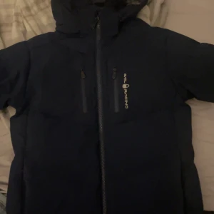 Mörkblå Sail Racing dunjacka & BOSS vindjacka - Två jackor säljes! En mörkblå dunjacka från Sail Racing med huva, dragkedja och logga på bröstet. Den andra är en marinblå vindjacka från BOSS med vit dragkedja, huva och två fickor med vita detaljer. Perfekta för kyliga dagar och blåsigt väder. Strl är 150