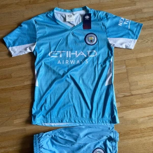 Manchester City Mahrez fotbollströja - Snygg Manchester City fotbollströja med Mahrez och nummer 26 på ryggen. Tröjan är ljusblå med vita detaljer och har klubbmärke samt Etihad Airways tryck på bröstet. Kortärmad modell i lätt och ventilerande polyester, perfekt för match eller träning.