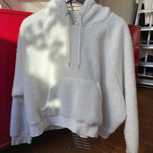 Vit fluffig hoodie med huva - Supermjuk och fluffig hoodie i vit färg med huva och snörning. Tröjan har en stor magficka och ribbade muddar vid ärmslut och nederkant. Perfekt för att chilla hemma. För liten för mig