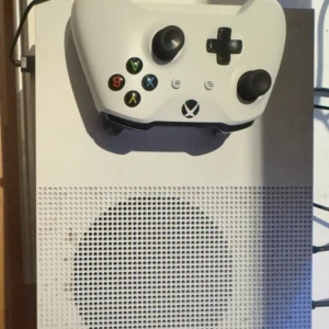 Xbox One S - Xbox One S i vitt med original handkontroll. Konsolen är i fungerande skick, startar utan problem och visas igång på TV. Viss smuts och mindre slitage syns på ovansidan, men inget som påverkar funktionen. Perfekt för gaming och streaming.