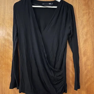 Svart omlottopp med v-ringning - Svart omlottopp från Lager 157 med djup v-ringning och långa ärmar. Toppens omlottdesign ger en snygg och smickrande figur.