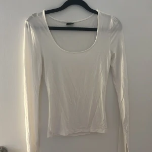 Vit långärmad topp från Gina Tricot - En stilren vit långärmad topp från Gina Tricot i storlek XS. Toppen har en djup rundad urringning och är figurnära i modellen. Perfekt att matcha med jeans eller kjol för en clean look.