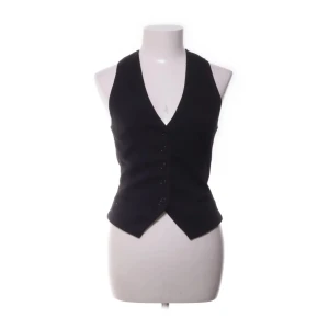 Svart kostymväst från H&M, storlek 34 - Klassisk svart väst från H&M med djup v-ringning och knappar framtill. Snygg figursydd passform och spetsig nederkant. Tillverkad i polyester, viskos och elastan för en bekväm känsla. Perfekt att styla över en skjorta eller t-shirt.💕