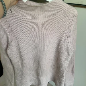 Ljusrosa stickad tröja med hög krage - Mysig ljusrosa stickad tröja med hög krage och långa ärmar. Tröjan har en enkel och clean design med bred ribbstickning och en något loose passform. Perfekt för kyliga dagar när du vill vara både bekväm och snygg.