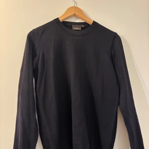 Mörkblå merinoull stickad tröja Oscar Jacobson - Svart stickad tröja från Oscar Jacobson med rund hals och lång ärm. Tröjan har en klassisk, enkel design och är tillverkad i mjukt stickat material som känns skönt mot huden. Perfekt för dig som gillar stilrena och tidlösa plagg. Merinoull nypris 1500
