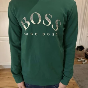 Grön långärmad tröja från Hugo Boss - Snygg grön långärmad tröja från Hugo Boss med stort BOSS-tryck på bröstet. Knappast använd.