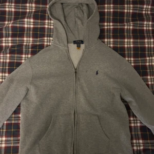 Polo Ralph Lauren hoodie - Grå hoodie från Polo Ralph Lauren med dragkedja framtill och klassisk blå logga. Passar 158-168 cm. Hör av vid frågor.
