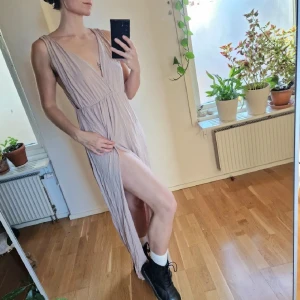 Beige långklänning från NLY Trend - Puder-rosa-beige, skulle jag vilja benämna färgen som. Hög slits, och riktigt härlig goddess-känsla. Jag trodde att den var med brun-beige när jag köpte den, så denna får vandra vidare eftersom jag inte är så bekväm med färgen 🧡 har tänkt sy den i området där jag nyper ihop den på bilden, men inte haft tid. Några stygn där och man slipper visa hela grenen 🙈 Återuppladdad för fri frakt. Jag har mycket annat uppe på sidan, både herr och damkläder. Köp gärna bundle för att få rabatt 🤗