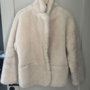 Beige teddyjacka från Lindex S - Supermjuk och fluffig teddyjacka från Lindex i beige färg. Jackan har hög krage, knäppning med knappar framtill och två fickor. Sparsamt använd så i bra skick.