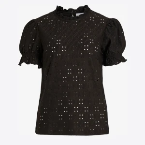 Svart blus med puffärm och spets!  - Svart blus med korta puffärmar och volangdetaljer vid ärmslut och hals. Blusen har ett broderat spetsmönster med små hål och en rundad halsringning (porto tillkommer) 