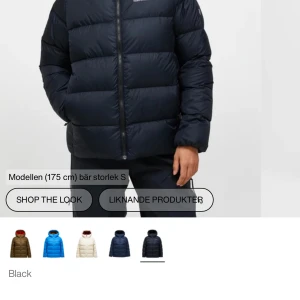 Svart dunjacka Peak Performance - Svart dunjacka från Peak Performance med huva och dragkedja. Jackan är quiltad och har en puffig siluett som ger en cool look. Perfekt för kalla dagar och har logga på bröstet samt ärmen. Klassisk modell med lång ärm och praktiska fickor. Har även några små smutsfläckar som går bort om man tvättar men även två små repor/hål se bild som säkert går att laga