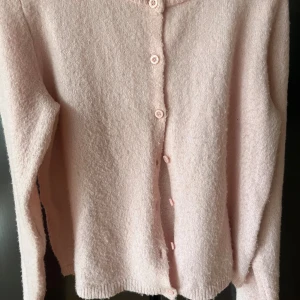 Ljusrosa kofta från 157  - Supermjuk ljusrosa kofta från 157 med rund hals och knappar. Koftan har långa ärmar samt ribbade muddar vid hals och ärmslut. Perfekt för lager-på-lager under kyliga dagar.