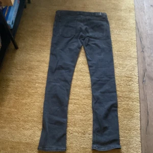 Svarta jeans från Nudie Jeans, 32/34 - Snygga svarta jeans från Nudie Jeans i klassisk femficksmodell. Jeansen har raka ben och normal passform, med subtila detaljer på bakfickorna och logotyp på insidan. Perfekt för dig som gillar stilrena och tidlösa jeans.