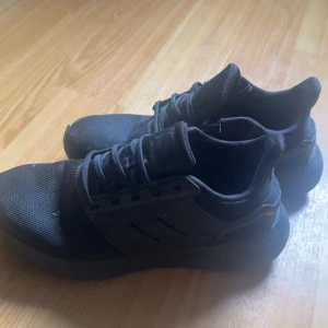 Svarta Adidas sneakers med mesh - Säljer ett par helsvarta Adidas sneakers i storlek 41 1/3. Skorna har en sportig look med ovandel i mesh och detaljer i syntet. Klassisk snörning och platt sula gör dem perfekta för en aktiv vardag. Diskret Adidas-logga på plösen.