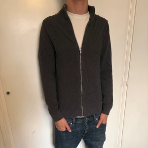 Mörkgrå kofta från Jack & Jones - Säljer en stilren mörkgrå kofta från Jack & Jones med hel dragkedja framtill. Skön och snyggt till hösten. [ storlek SX men sitter som S ] Hör av er vid minsta fundering!