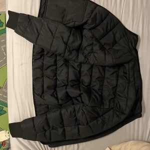 Svart pufferjacka från Replay, stl S - Säljer en svart pufferjacka från Replay i storlek S. Jackan är quiltad, har ribbade muddar vid ärmsluten och dragkedja framtill. Tillverkad i lättviktig polyester och har en clean, modern look. Perfekt för kalla dagar när du vill hålla stilen. Är aldrig använd.