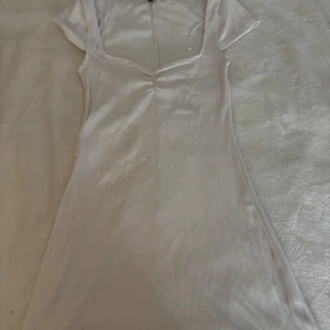 Vit klänning - Supersöt vit kortklänning med ribbad struktur och v-ringad hals. Klänningen har korta ärmar och en lätt figurnära passform som ger en snygg siluett. Perfekt för dig som gillar stilrena och enkla plagg med en feminin touch.