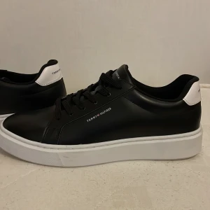  Tommy Hilfiger skor - Stilrena svarta sneakers från Tommy Hilfiger med vit tjock sula och vit detalj på hälen. Skorna har snörning och är tillverkade i syntetmaterial med diskret logga på sidan och bak. Perfekta för dig som gillar en clean och modern look. Använt bara 1 gång 