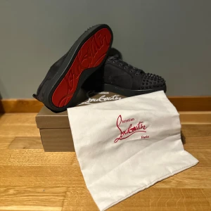 Christian Louboutin skor - Gråa sneakers från Christian Louboutin i mocka med ikoniska röda sulor och gråa nitar på tån. Skorna har snörning och rund tå, samt exklusiv känsla med lyxiga material och detaljer. Perfekta för dig som vill sticka ut med en edgy och trendig look.