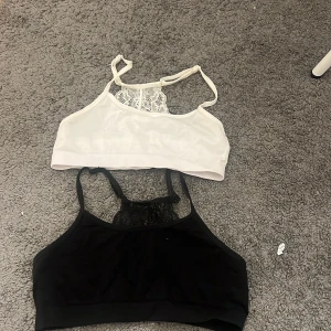 Svart och vit linnetopp med spets - Två snygga linnetoppar i svart och vit med smala axelband och dekorativ spetsdetalj framtill. Perfekt för att ge en extra touch till din outfit. Mjukt material och stilren design som passar till många looks.