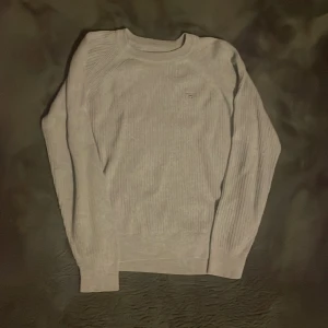 Ljusgrå tröja från GANT - Säljer en ljusgrå stickad tröja från GANT med ribbad struktur och broderad logga på bröstet. Tröjan har rund halsringning.