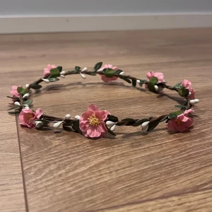 Sommardiadem! - Ett fint diadem med konstgjorda rosa blommor och gröna blad, perfekt för midsommar eller festival. Diademet har en tunn brun stomme dekorerad med små vita knoppar och detaljerade blommor! 🌸 