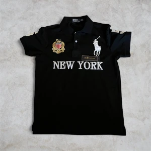 Svart Polo Ralph Lauren piké New York - Svart pikétröja från Polo Ralph Lauren med broderad New York-text, emblem och klassisk polospelare på bröstet. Custom fit-modell med krage och knappar framtill. Inte autentisk men ser sjukt bra ut. Chief keef type shit.