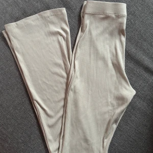 Beige ribbade byxor från Divided XS - Säljer ett par ljusbeige ribbade byxor från Divided i storlek XS. Byxorna har raka ben, hög midja och är tillverkade i ett stretchigt material med 87% polyester och 13% elastan. De har ett diskret randigt mönster och är superbekväma.