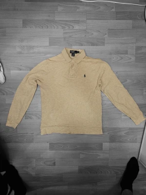 Beige långärmad pikétröja Polo Ralph Lauren - Säljer en beige långärmad pikétröja från Polo Ralph Lauren. Tröjan har klassisk krage, knappar vid halsen och den ikoniska broderade loggan på bröstet. Perfekt för dig som gillar stilrena och tidlösa plagg.