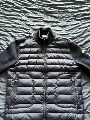 Svart Moncler cardigan  - Säljer en svart cardigan från Moncler med quiltad front och stickade ärmar samt rygg. Jackan har dragkedja framtill, två fickor med dragkedja och hög krage. Perfekt för dig som vill ha en clean och stilren look med premiumkänsla. Säljer den då den inte passar. Vid snabb affär kan jag sänka priset 🤗
