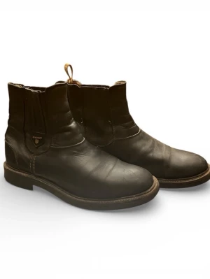 Svarta chelsea boots från Gant - Säljer ett par klassiska svarta chelsea boots från Gant i skinn. De har elastiska paneler på sidorna, dragflikar bak och en robust sula. Perfekta för dig som gillar stilrena boots med en tidlös look.