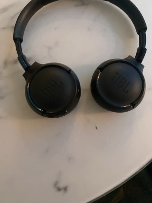 JBL trådlösa over-ear hörlurar - Snygga svarta JBL over-ear hörlurar i gott skick. Trådlös design för bekväm användning, mjuka öronkuddar och justerbar bygel. Perfekta för musik, film och samtal. Inga synliga defekter eller större slitage.