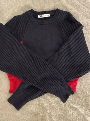 Marinblå och röd stickad tröja från Zara - Säljer en marinblå och röd stickad tröja från Zara. Tröjan har ribbade långärmar och sidor i rött, medan resten är svart. Rund halsringning och mjukt material som känns skönt mot huden. Perfekt för dig som gillar kontraster och vill sticka ut lite extra. Är i storlek m men skulle liten i storlek så mer åt xs/s