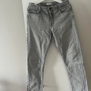 Grå jeansbyxor från Jack & Jones  - Snygga grå jeans från Jack and Jones. Perfekta för en avslappnad stil med klassiska femficksdetaljer och knappgylf.
