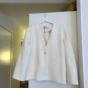 Kort vit kappa, storlek M - Säljer en superfin krämvit kappa från bikbok i storlek M. Aldrig använd så kappan är i nyskick, med lappen kvar. Rak passform, V-ringning och diskret knapp framtill. Passar jättebra till både jeans, kostymbyxor eller klänning!💕