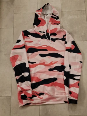 Hoodie rosa - Hoodie rosa. Modehuva, Casual sportströja i svart camo med framficka. Stretchblandning. Polyester. Lämplig för vår och höst. Maskintvättbar.  Perfekt för daglig användning.