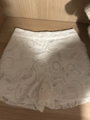 Vita spetsiga shorts med broderi - Nypris 20€! Prislapp kvar!!Säljer ett par vita shorts med snyggt broderat spetsmönster och fodrad insida. De har hög midja och en feminin, elegant look med fina detaljer i spetsen. Perfekta för sommarens alla tillfällen!