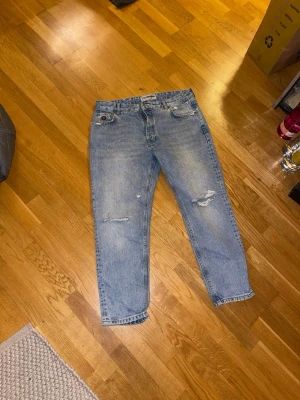 Zara RHUIGI blå jeans med slitningar - Säljer ett par blå jeans från Zara RHUIGI med snygga slitningar på benen och broderad detalj vid fickan. Jeansen har klassisk femficksdesign, raka ben och är gjorda i robust denim. Perfekta för dig som gillar en avslappnad och trendig look.