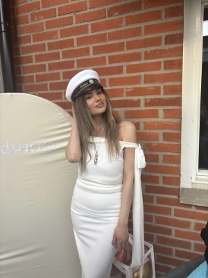 Vit axelbandslös långklänning - Supersnygg vit långklänning med offshoulder och en stor rosett på ena armen. Klänningen har en tight passform och är perfekt för student eller sommarens alla tillfällen. Materialet känns mjukt och följsamt.