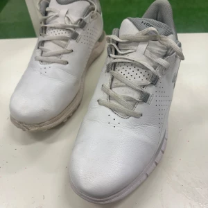 Vita golfskor från Under Armour - Säljer ett par vita golfskor från Under Armour med grå detaljer och snörning. Skorna har perforerade partier för ventilation, vadderad häl och robust sula med grepp. Materialet är syntet och skinn, perfekt för golfbanan. Diskret logga på sidan och tungan.